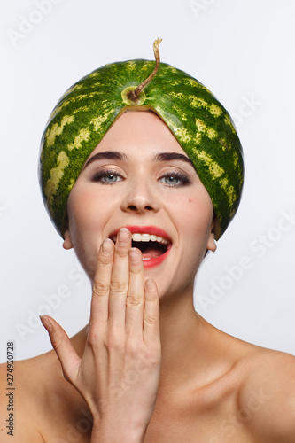 Creative portrait of a woman with a watermelon on her head instead of a hat. White background