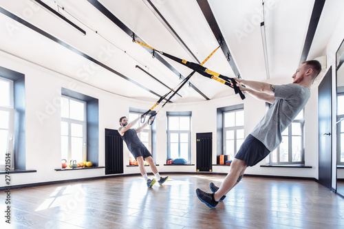 Two strong male athletes are engaged in the hall with to the trx system. Concept of team spirit and the trend of a healthy lifestyle