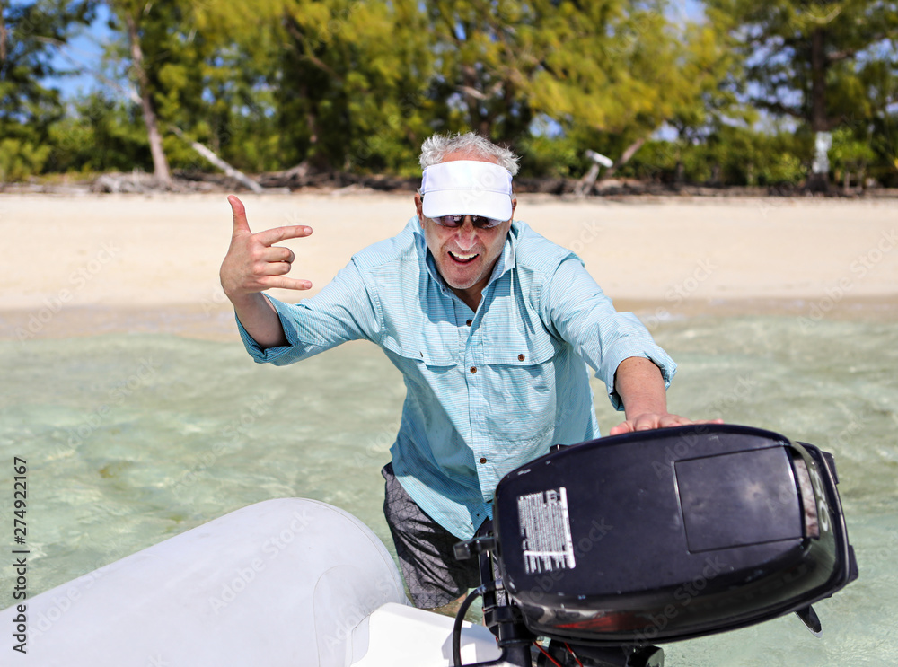 Naklejka premium Older man pushing his dinghy out to get it started off the beach 