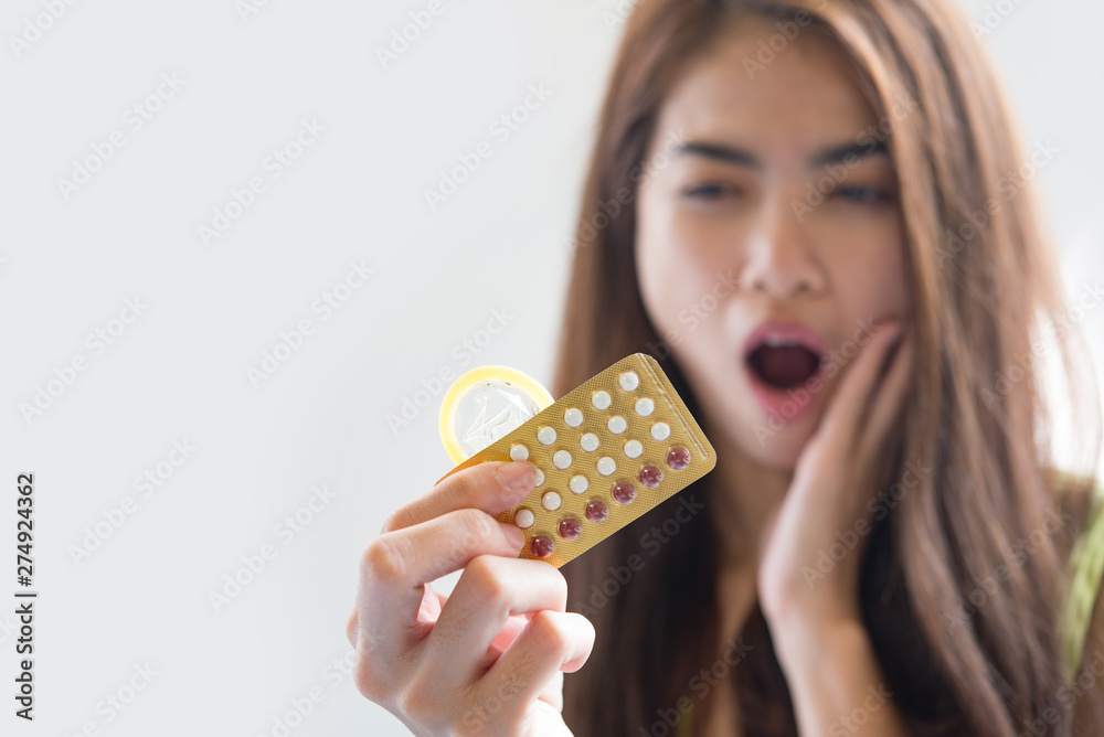 Young woman holding condom and contraceptive pills prevent pregnancy Young woman holding condom and contraceptive pills prevent pregnancy