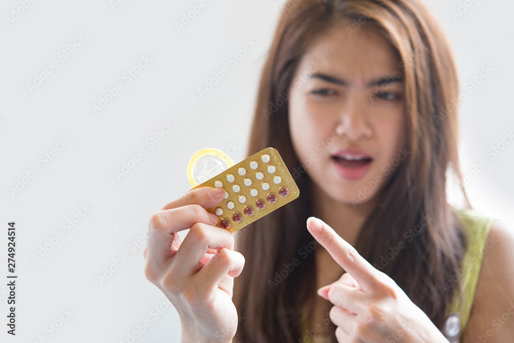 Young woman holding condom and contraceptive pills prevent pregnancy Young woman holding condom and contraceptive pills prevent pregnancy