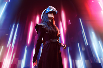 Beautiful woman in futuristic dress over dark background. Girl in glasses of virtual reality. Augmented reality, game, future technology, robots and people concept. VR. Neon light.