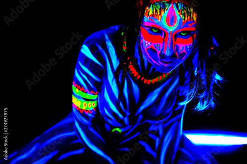 Portrait of Wild and frantic Young naked bodyarted woman in blue glowing ultraviolet paint and Yellow eye lenses. Avatar entity amazon warrior girl with pigtails hairstyle