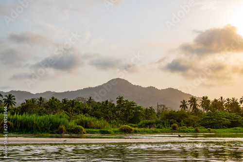 A wide river flows through the tropical rainforest of South America at a beautiful sunset where people bathe and enjoy life, Colombia Palomino