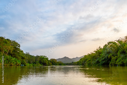 A wide river flows through the tropical rainforest of South America at a beautiful sunset where people bathe and enjoy life  Colombia Palomino