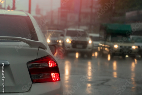 Blurred image from rainy season. The back of the white car parked on the traffic signal and there are many cars on the opposite side. Turn on the light for safety.