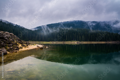 Montenegro, Rocky beach of black lake reflecting foggy trees and forest in calm waters in perfect paradise like nature landscape of durmitor national park near zabljak