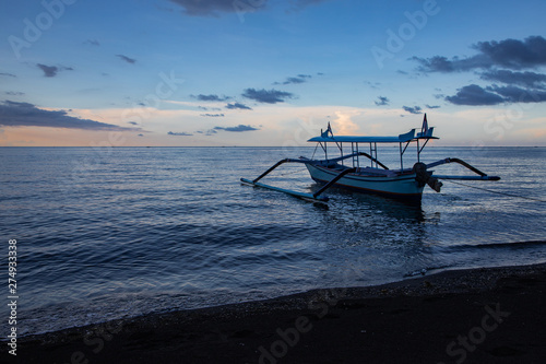 Blue hour over calm ocean and black sand beach with balinese boat