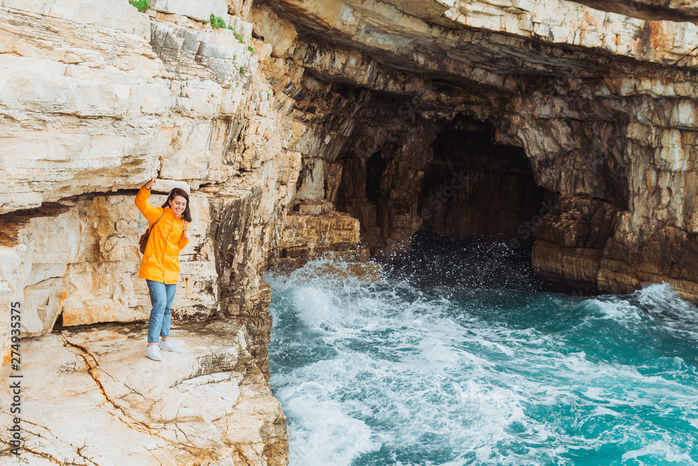 woman in yellow raincoat standing on the cliff looking into grotto