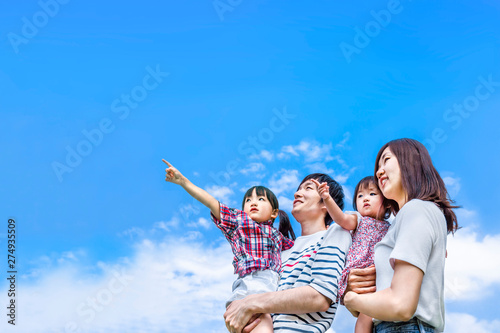 青空をバックに遠くを見つめ指さす4人家族。幸せ、希望、愛情、育児イメージ