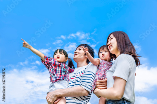 青空をバックに遠くを見つめ指さす4人家族。幸せ、希望、愛情、育児イメージ © chikala