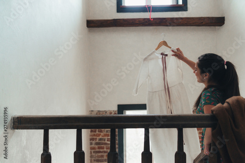 Girl is gathering for a walk. Husband is waiting for wife. Female is preparing for a date. Dressing a newly-married couple. Woman holding white dress on a stairs