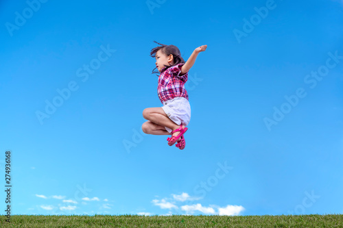 緑の芝地で青空をバックにジャンプする幼い女の子。元気、パワフル、努力イメージ
