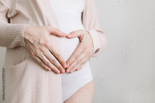 Pregnant Woman holding her hands in a heart shape on baby bump. Pregnant Belly with fingers Heart symbol. Maternity concept. Baby Shower 