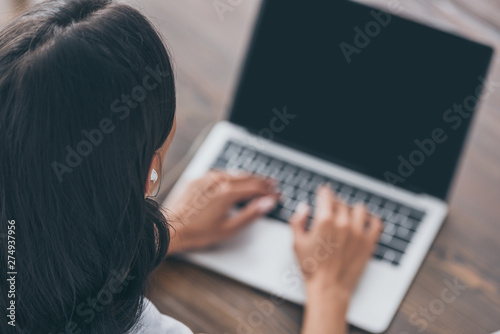 overhead view of young woman in earphones using laptop while sitting at wooden table