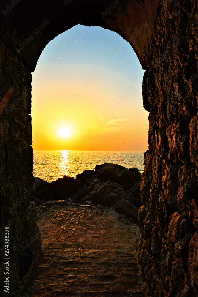 Setting sun through an ancient stone archway over the Mediterranean Sea