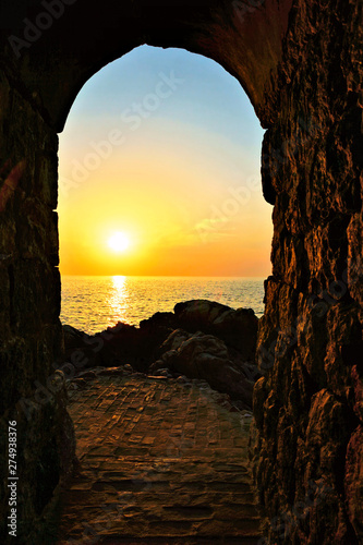 Fototapeta Naklejka Na Ścianę i Meble -  Setting sun through an ancient stone archway over the Mediterranean Sea