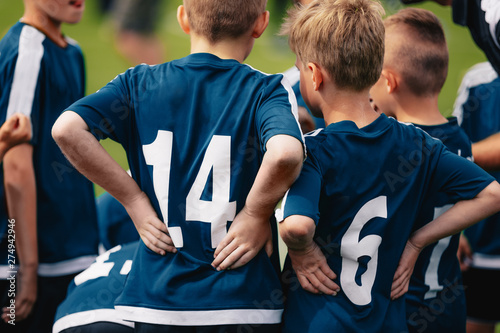 Children in soccer team. Young boys standing in a team with coach. Close-up of football team standing back. Young footballers in jersey shirts with numbers