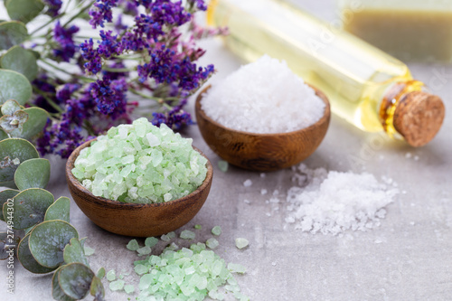 Sea salt in bowl  aroma oil in bottles  Wellness and flowers on grey textured background and flowers on vintage wooden background. Selective focus.