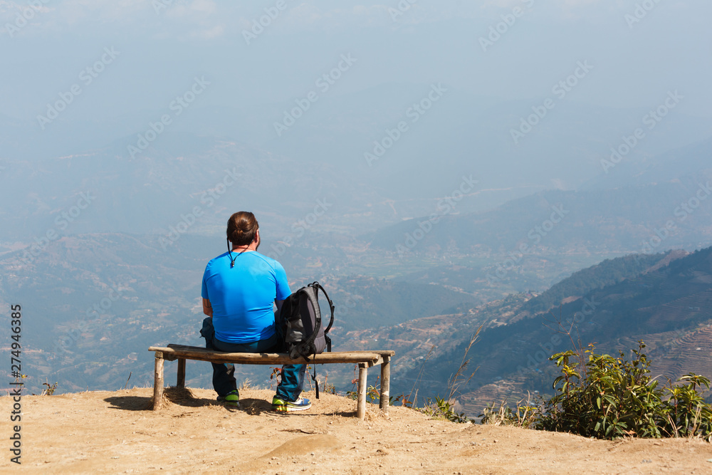 A man with a backpack sits on a bench looking to the horizon. Kathmandu. Nagarkot. View point on the mountains of Nepal. Landmark.