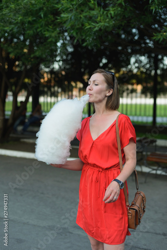 young adult asian woman in red dress eating cotton candy at amusement park, vertical lifestyle stock photo image