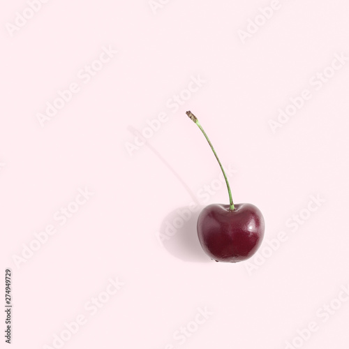 One ripe berry of a sweet cherry with a stem is on a light pink background. Flat lay, top view minimal composition.