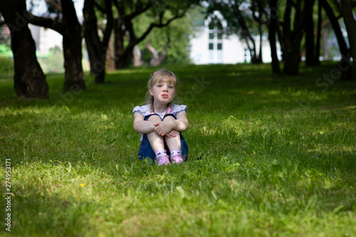 Sweet, happy little girl sitting on a grass in a park