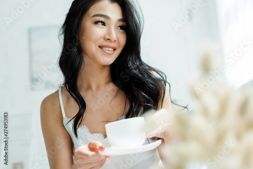 selective focus of positive thai woman holding cup with tea