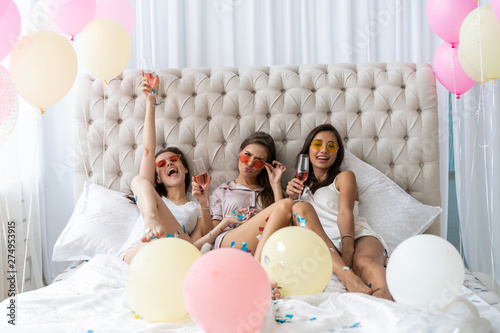 Pajama party. Attractive young smiling women in pajamas drinking champagne while having a slumber party in the bedroom.