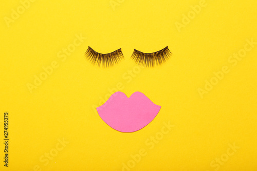 Makeup eyelashes and pink paper lips on yellow background. Minimalism concept