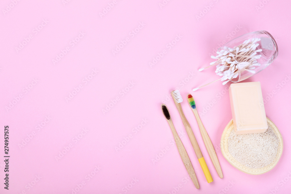 Bamboo toothbrushes with cotton sticks, soap and washcloth on pink background
