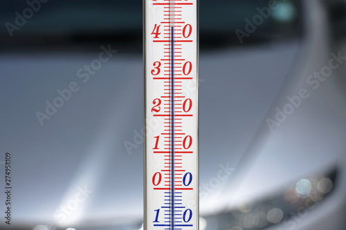 Thermometer during hot weather with car in background