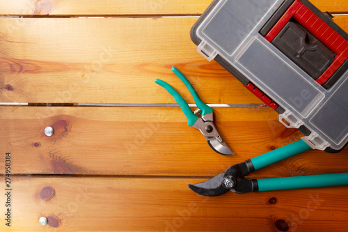 Two pairs of pruning scissors and a tool box are laying on a wooden surface