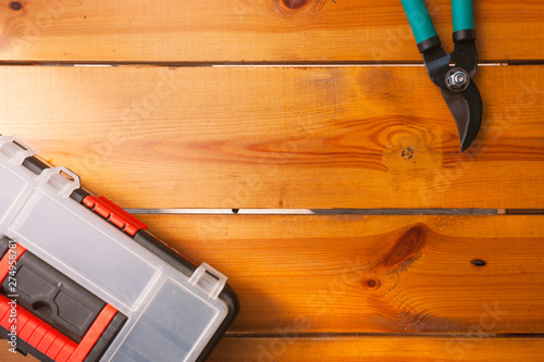 Two pairs of pruning scissors and a tool box are laying on a wooden surface
