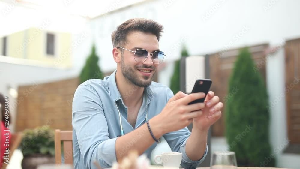 smiling casual man sits at restaurant and reads feed on his mobile phone while drinking his coffee and enjoys his time off