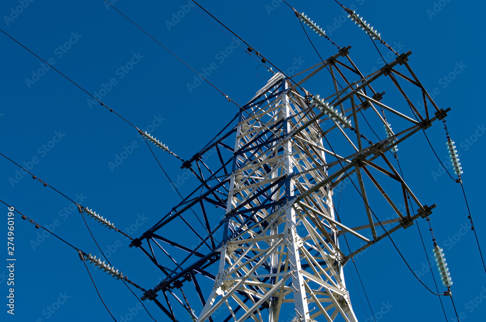 The white metal structure with bulkheads is a power transmission tower equipped with extensions and dielectric insulators with cables against a blue sky The white metal structure with bulkheads is a power transmission tower equipped with extensions and dielectric insulators with cables against a blue sky