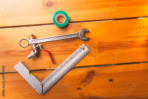 A ruler, tape, a wrench, and piping is laying on a wooden surface
