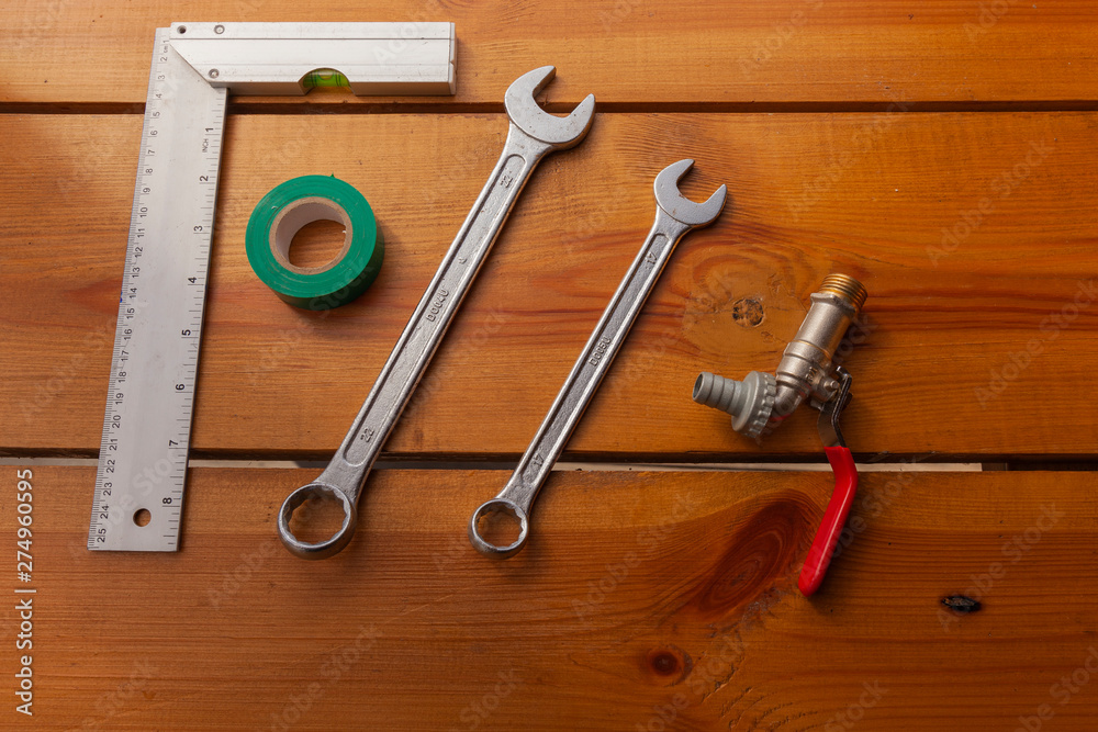 A ruler, tape, a wrench, and piping is laying on a wooden surface A ruler, tape, a wrench, and piping is laying on a wooden surface