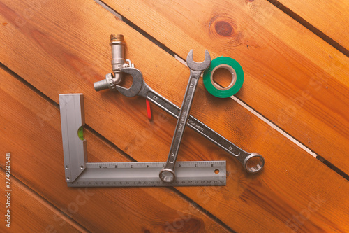 A ruler, tape, a wrench, and piping is laying on a wooden surface