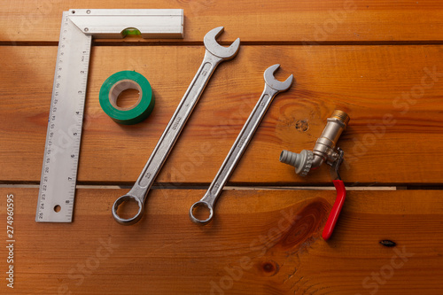 A ruler, tape, a wrench, and piping is laying on a wooden surface