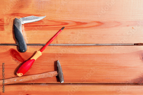 A pocket knife, screwdriver, and a hammer are laying on a wooden surface