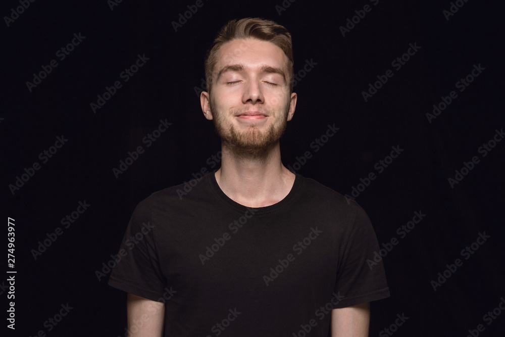 Close up portrait of young man isolated on black studio background. Photoshot of real emotions of male model with closed eyes. Thinking and smiling. Facial expression, human emotions concept. Close up portrait of young man isolated on black studio background. Photoshot of real emotions of male model with closed eyes. Thinking and smiling. Facial expression, human emotions concept.