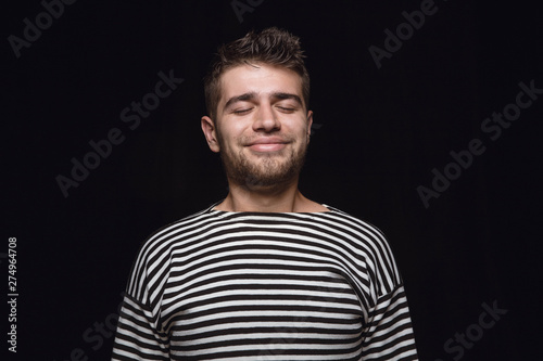 Close up portrait of young man isolated on black studio background. Photoshot of real emotions of male model with closed eyes. Thinking and smiling. Facial expression, human emotions concept.