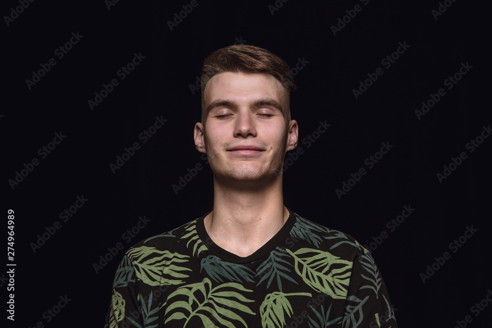 Obraz premium Close up portrait of young man isolated on black studio background. Photoshot of real emotions of male model with closed eyes. Thinking and smiling. Facial expression, human emotions concept.