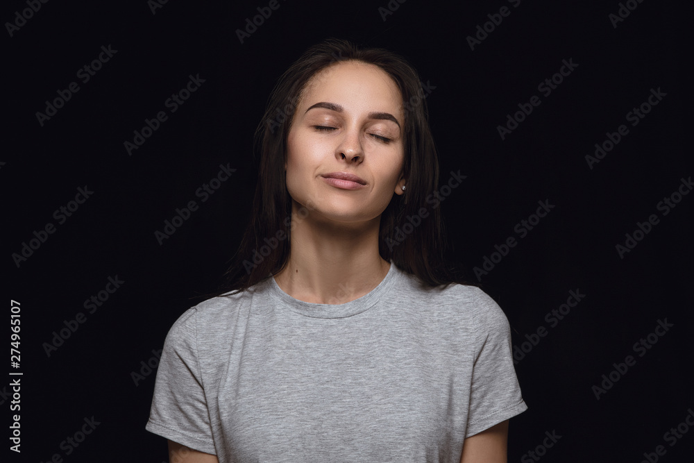 Fototapeta premium Close up portrait of young woman isolated on black studio background. Photoshot of real emotions of female model with closed eyes. Thinking and smiling. Facial expression, human emotions concept.