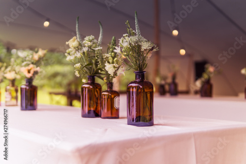 Image of modern wedding decoration with flowers in brown bottels and blurry lights in the background