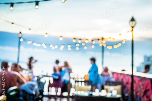 Defocused people attending open air summer party on the roof top. Warm sun light in the evening.