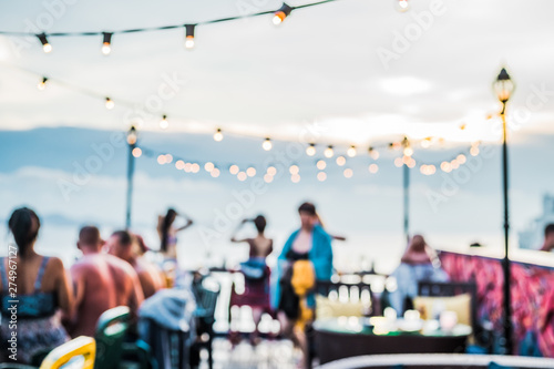 Defocused people attending open air summer party on the roof top. Warm sun light in the evening.