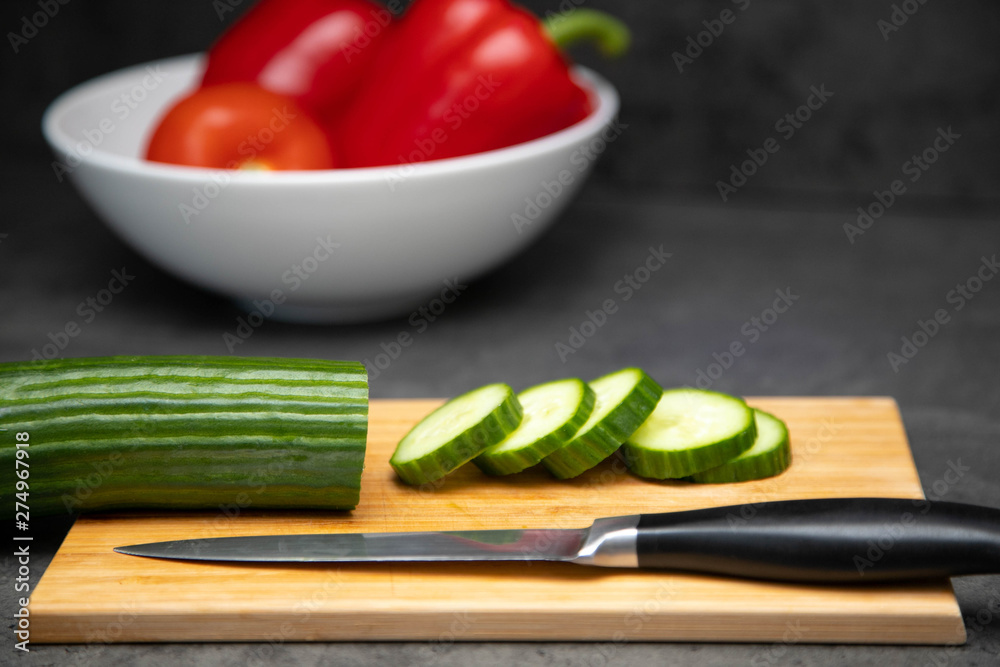 sliced fresh cucumber on a cutting board with a knife and a ceramic plate of vegetables. sliced fresh cucumber on a cutting board with a knife and a ceramic plate of vegetables.