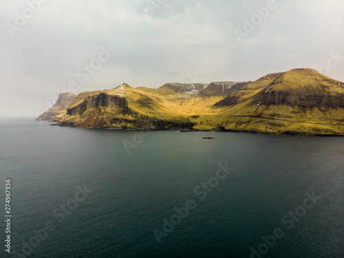 Aerial view of Faroese coastline above Drangarnir and Tindholmur island with view towards the village Bour with snow-covered mountains (Faroe Islands, Denmark, Europe)